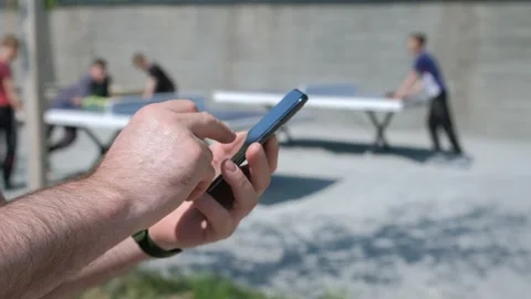 The male on a bench, and scrolls through the pictures in the phone, on promenade Stock Footage 256208774