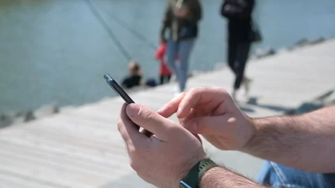 The male on a bench, and scrolls through the pictures in the phone, on promenade Video stock 256208963