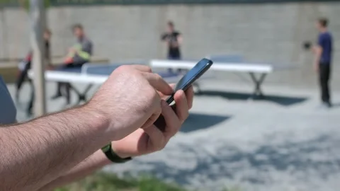 The male on a bench, and scrolls through the pictures in the phone, on promenade Stock Footage 257460550