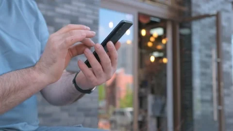 The male on a bench, and scrolls through the pictures in the phone, on promenade Stock Footage 258655543