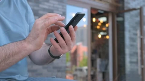 The male on a bench, and scrolls through the pictures in the phone, on promenade Stock Footage 267864939