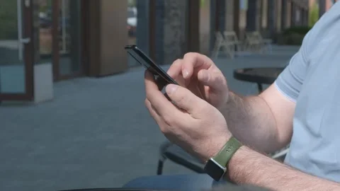 The male on a bench, and scrolls through the pictures in the phone, on promenade Stock Footage 277741241