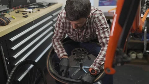 Male bicycle mechanic working in workshop. Bike repairman changing tire on Stock Footage 255842771