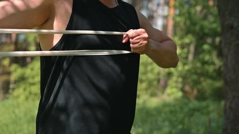 A male in a black tank top performs strength exercises with resistance bands in Stock Footage 339016241