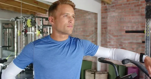 Male in blue shirt, white arm sleeves leaning on cardio handle, camera moving, Vidéo 340882353