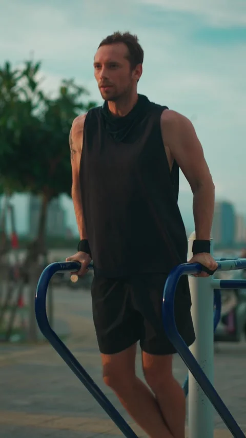 Male bodybuilder performing dips on parallel bars during sunset workout, Athlete 動画素材 316791375