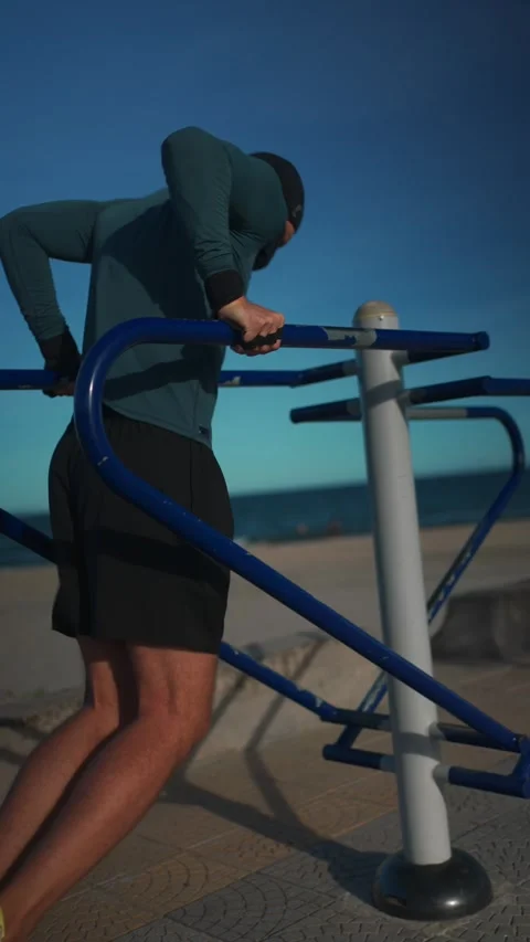 Male bodybuilder performing dips on parallel bars during sunset workout Stock Footage 320520866