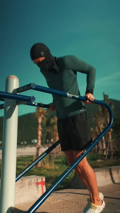 Male bodybuilder performing dips on parallel bars during sunset workout, Athlete Stock Footage 320525124