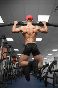 A male bodybuilder performs pull-ups on a horizontal bar in the gym. Stock Photos