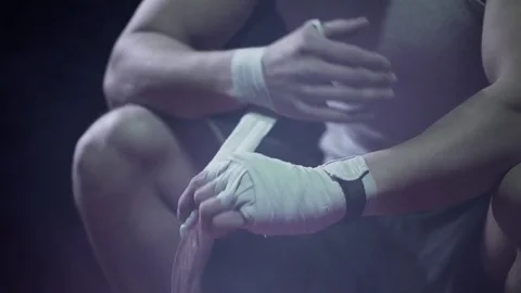 Male boxer wraps his hands with bandages before the fight training. It's a dark Stock Footage 80862256