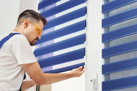 Male builder carpenter pulling down a blue jalousie on a window. Repairing and Foto stock