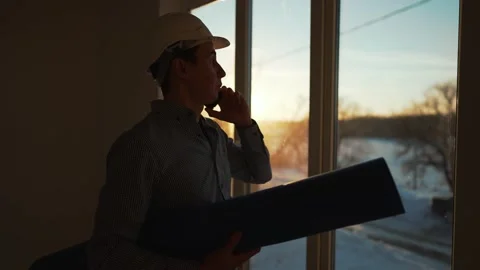 Male builder in hard hat stands at window, silhouette. Business concept of an Stock Footage 236743746