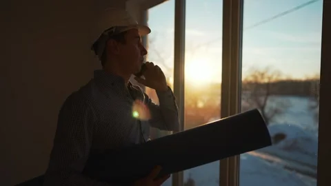 Male builder in hard hat stands at window, silhouette. Business concept of an Stock Footage 241500971