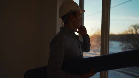 Male builder in hard hat stands at window, silhouette. Business concept of an Stock Footage 252109277