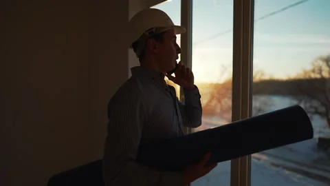 Male builder in hard hat stands at window, silhouette. Business concept of an Stock Footage 258208073