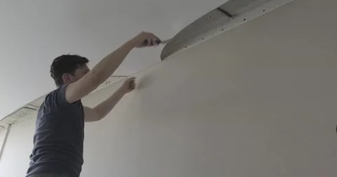 Male builder pulls glossy ceiling, works, trowels fabric of ceiling with spatula Stock Footage 131036255