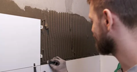 Male builder with thick beard sets guidelines for laying tiles in bathroom Stock Footage 130777325