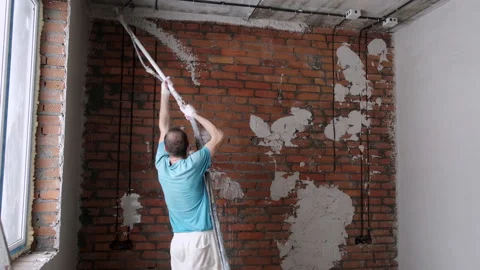 Male Builder uses Spray Bottle to Apply Mortar to Brick Wall. Liquid Plaster Stock Footage 168354574