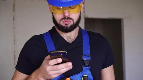 A male builder is using a smartphone. Worker at a construction site is holding a Stock Footage 131095655