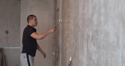 Male builder working at construction site, applying with roller white putty Stock Footage 129837591