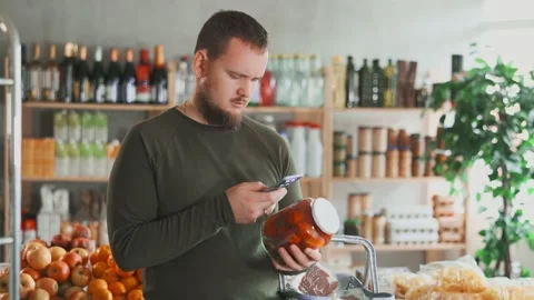 Male buyer scans the qr code on a glass jar with marinated tomatoes with a Stock Footage 314762581
