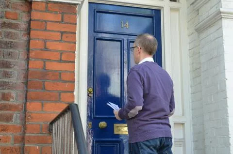Male canvasser knocking on a blue door and standing outside Stock Photos