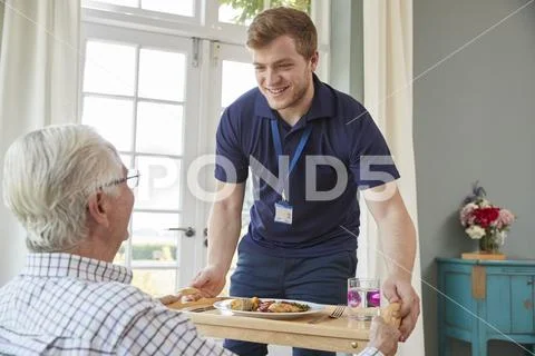 Male care worker serving dinner to a senior man at his home Stock Photos