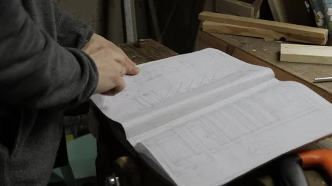 Male carpenter checking the notebook for blueprints of wooden constructions Vidéo 119669577