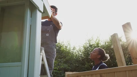 Male Carpenter With Female Apprentice Putting Roof On Outdoor Summerhouse In Stock-Footage 124569549