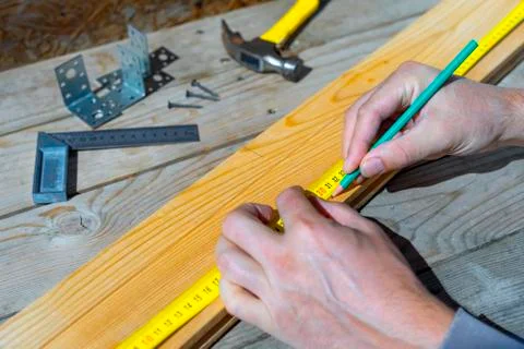 Male carpenter notes with pencil using measuring tape on the board, marks for Stock Photos