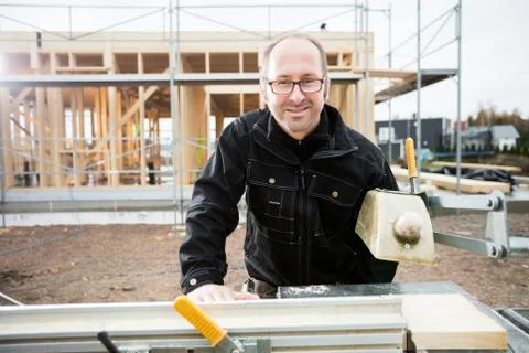 Male Carpenter Smiling While Using Table Saw To Cut Plank Foto stock
