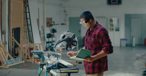 Male carpenter working in the workshop while wearing goggles and writing on the Stock-Footage 199621254