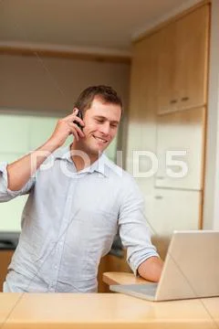Male with cellphone and laptop in the kitchen Stock-Fotos