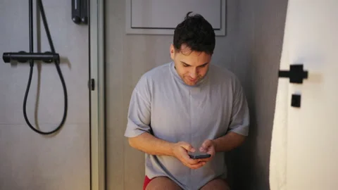 Male checking phone while sitting in restroom Vídeos de archivo 342952535