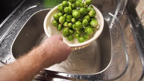 A male chef hand uses a plastic colander to rinse a pile of brussel sprouts unde Stock Footage 301919733