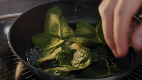 Male chef hands adding fresh spinach leaves to a frying pan in slow motion Stock-Footage 150714567