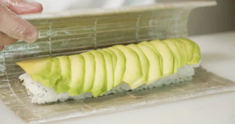 Male chef hands in gloves preparing delicious sushi rolls with avocado Stock Footage 135510919