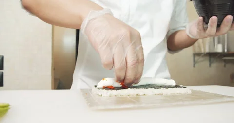 Male chef hands in gloves preparing sushi rolls with soft cheese and tobiko Stock Footage 135580893