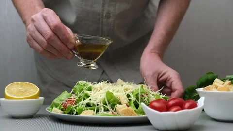 A male chef prepares a Caesar salad. Pours sauce over the salad. Recipe. Step 5. Stock Footage