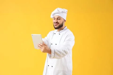 Male chef using tablet computer on yellow background Stock Photos