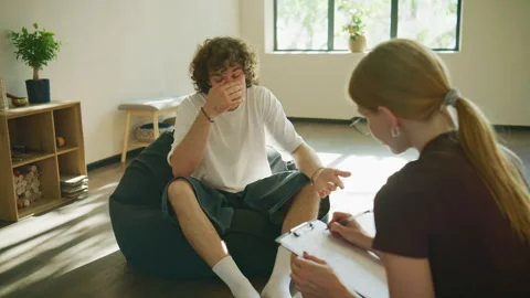 A male client sits angrily in therapy, raising his voice as he complains to the Stock Footage 345017270
