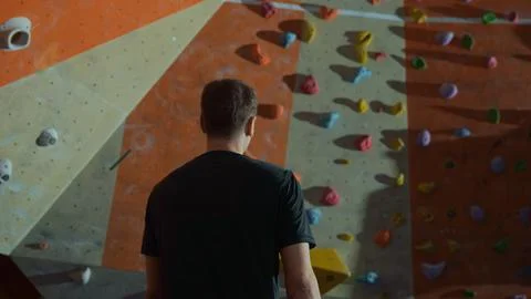 A male climber with his back to the camera walks towards the climbing wall Stock Photos