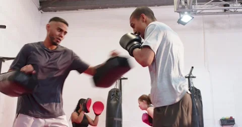 Male coach and trainee training with shifting pads in boxing gym as female Stock Footage 345070225