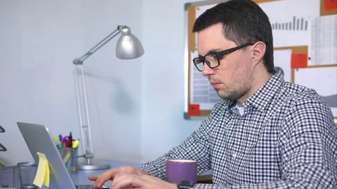Male computer user typing on keyboard, looking at the screen and drinking coffee Stock Footage 75486071
