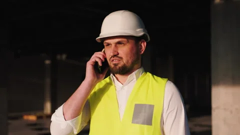 A male construction worker in a hard hat and neon safety vest is standing on a Stock Footage 283933164