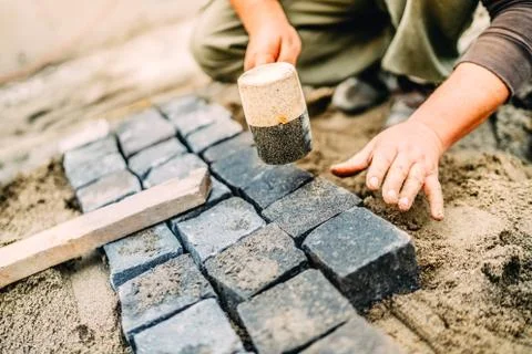 Male construction worker using granite cobblestone blocks to create path Stock Photos