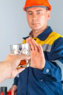 A male construction worker in work clothes refuses a glass of whiskey at work Stock Photos