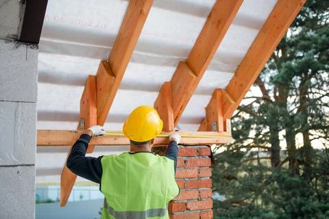 Male constructor secures ridge beam at roof peak, timber lags visible, adva.. Stock-Fotos