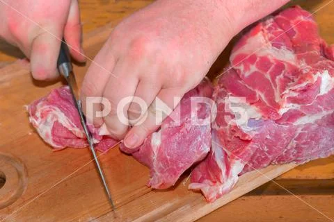 A male cook cuts a piece of juicy pork meat for a barbecue. Stock Photos