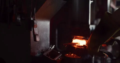 Male craftsman using a machine to press a piece of red hot iron in interior blac Stock Footage 199463157